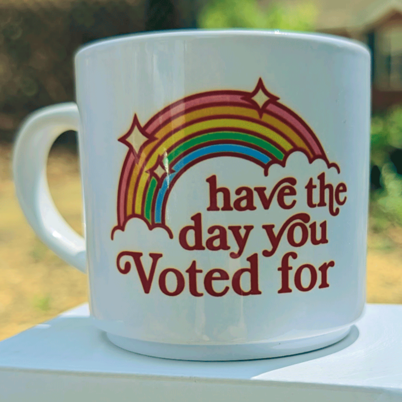 White mug with a rainbow design and the words, "have the day your voted  for"